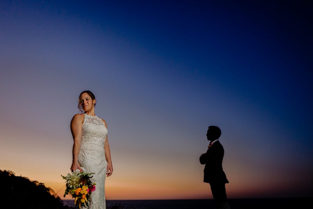 bride and groom at sunset the bride are holding flowers and the groom is in the background 