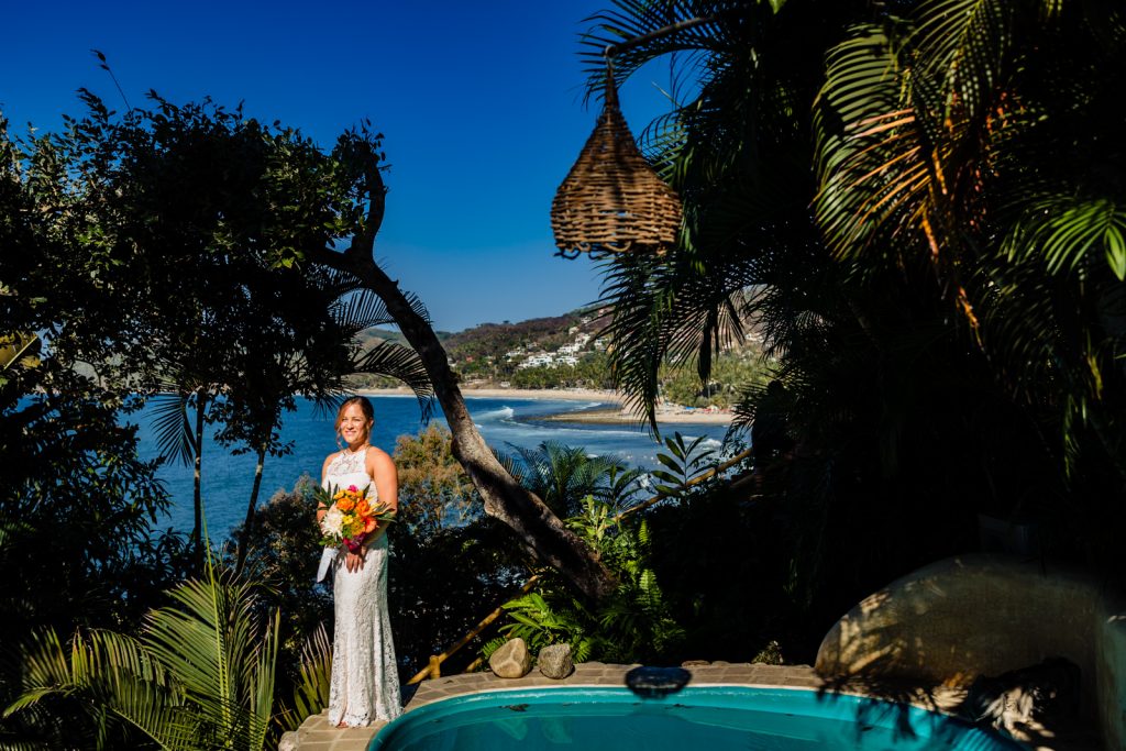 bride by the pool with flowers with the ocean on the background in sayulita