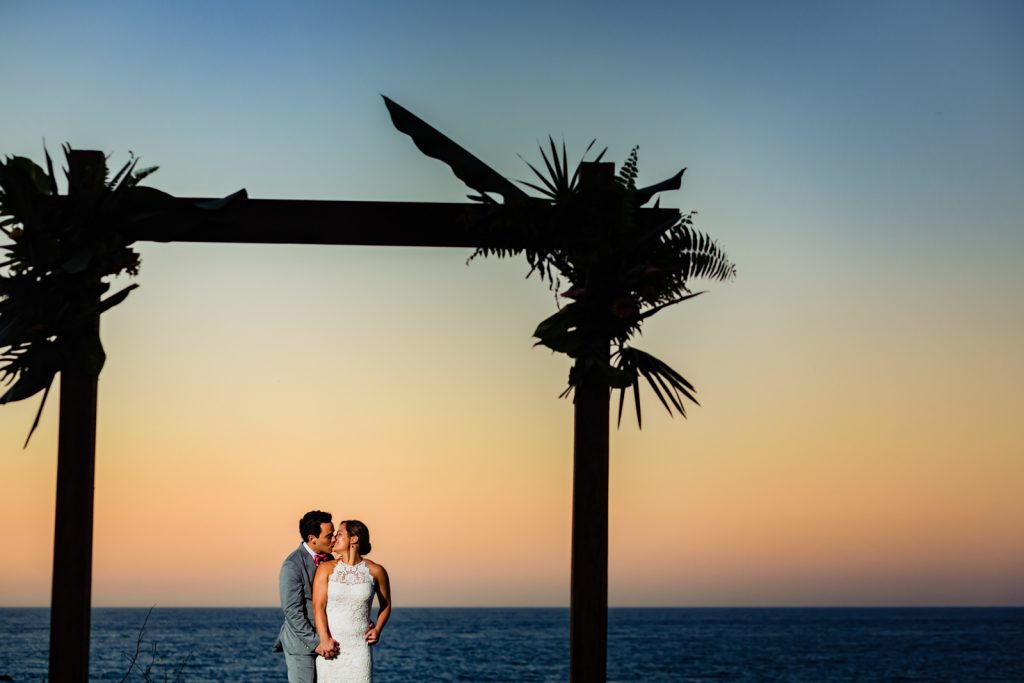 bride and groom kissing during the sunset with the ocean on the background