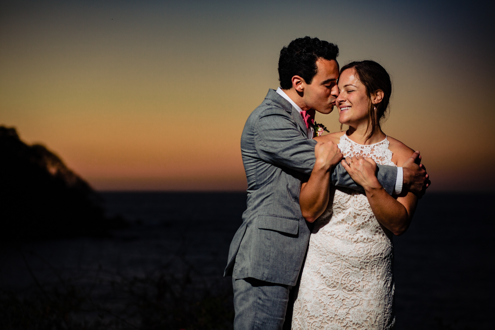 bride and groom hugs at the sunset the groom kiss her and the bride smile