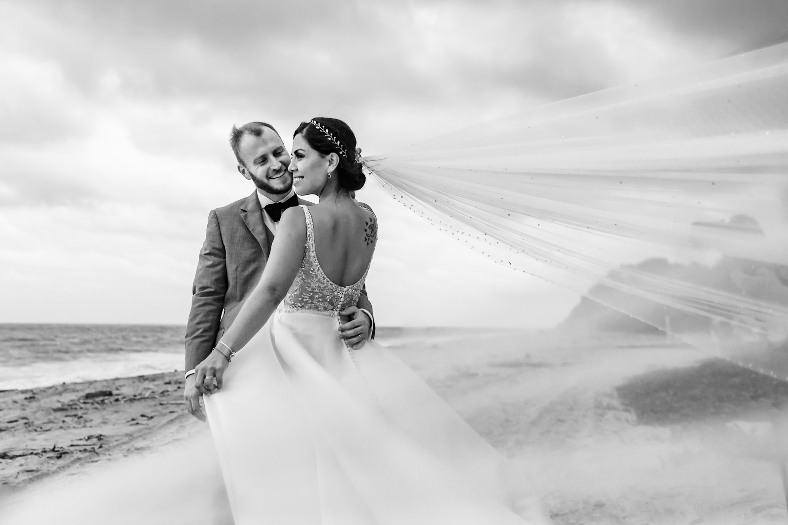 bride and groom on the beach play with the veil