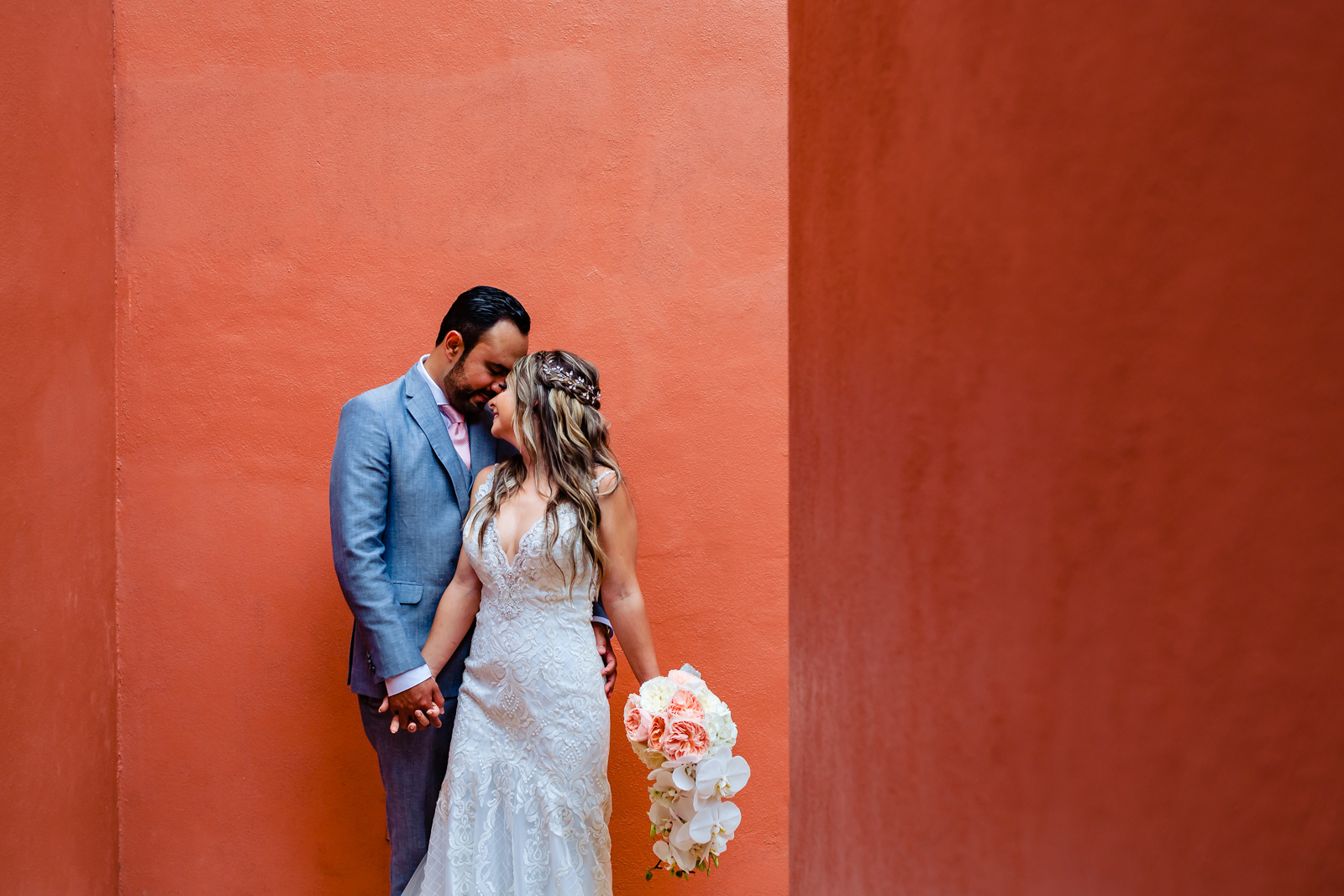 bride and groom hugs and touch his face on a red wall