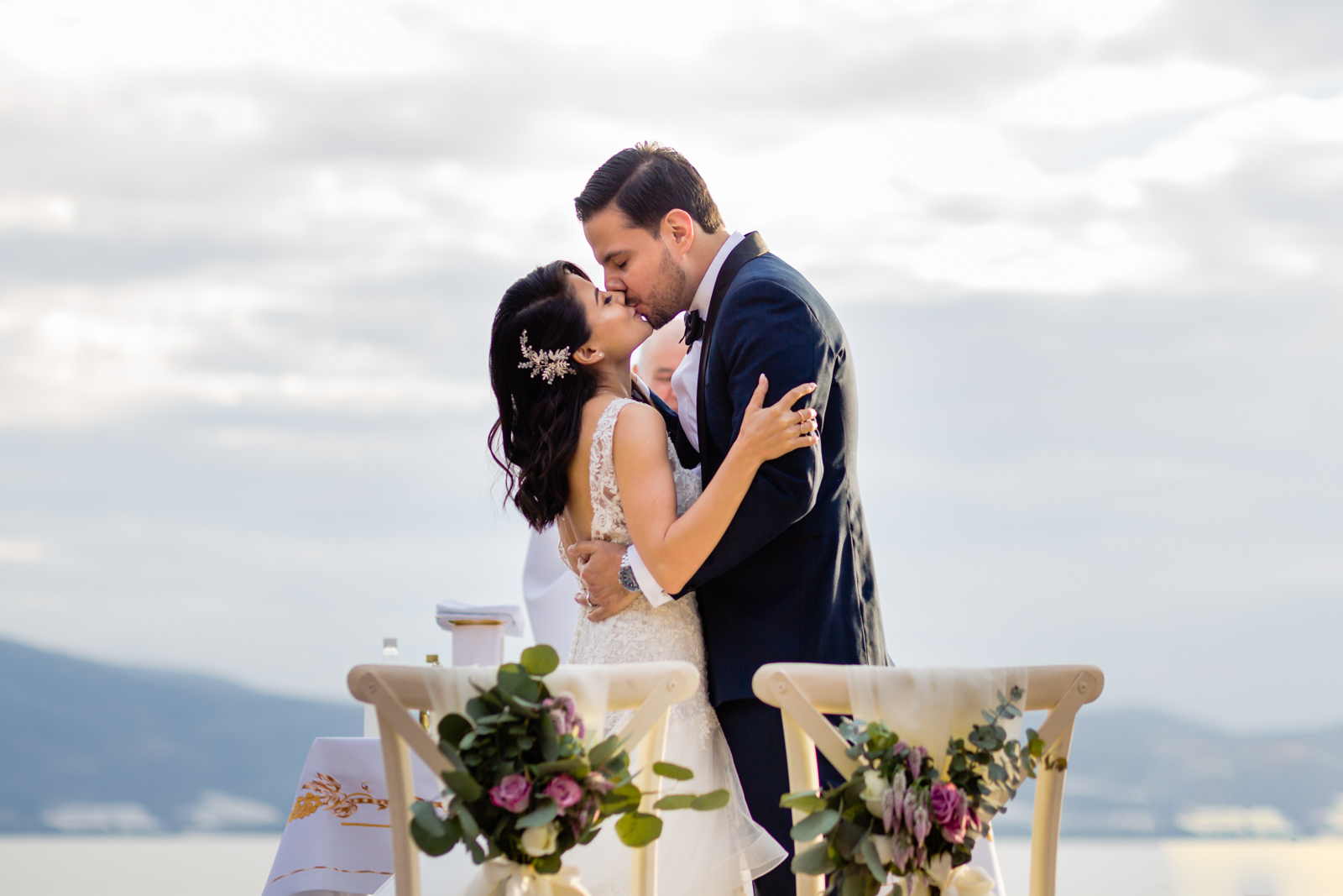 bride and groom first kiss during the ceremony with the lake on the background 