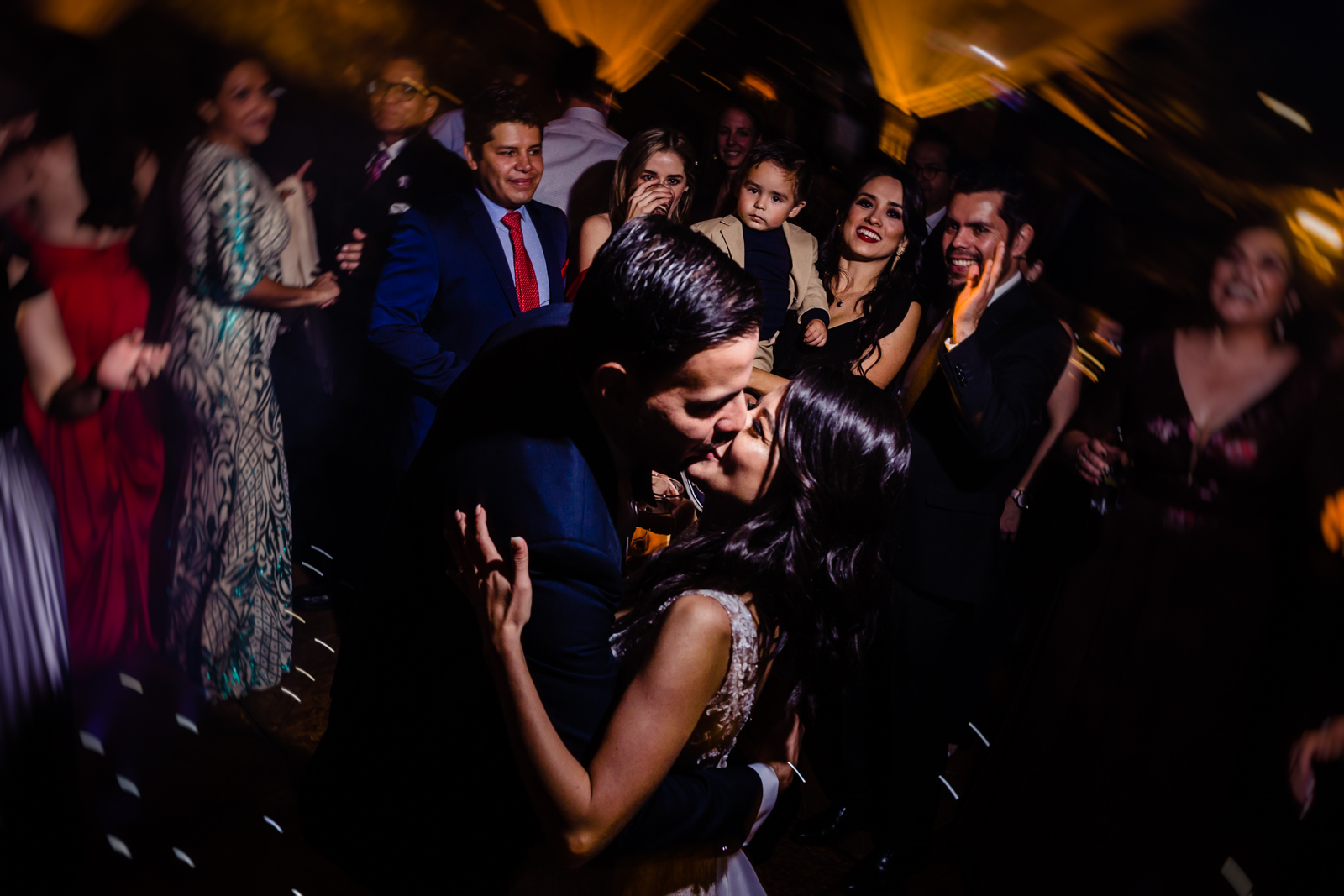 bride and groom kiss with all the friends behind them on the dance floor 