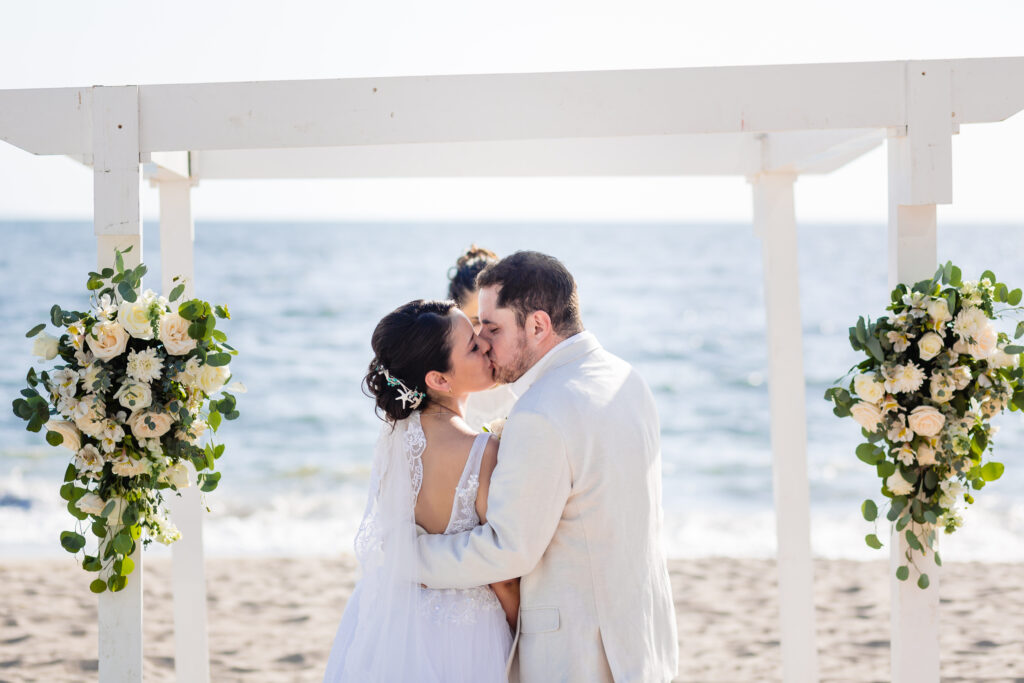 bride and groom kissing for the first time after the ceremony with the ocean on the background