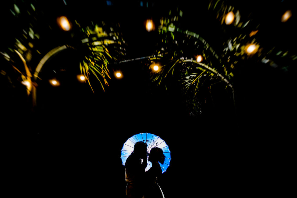 bride and groom holding a umbrella and looking at each other with lights above them