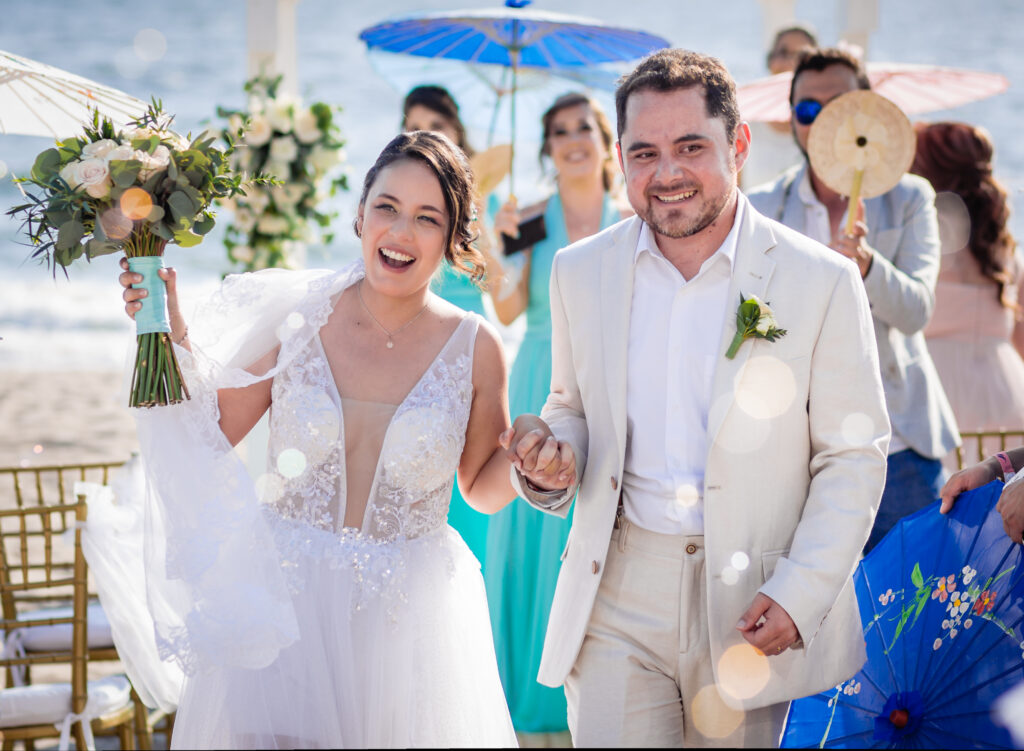 bride and groom holding hands and walking together after the ceremony on the beach the bride with a bouquet through the soap bubble 