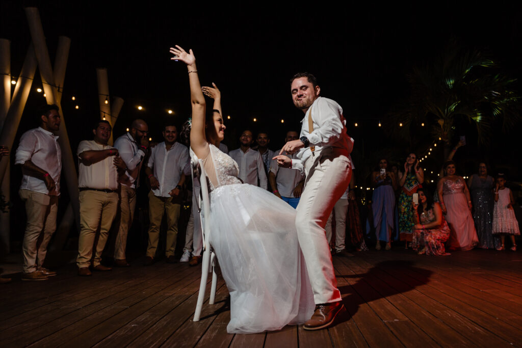 bride sit on a chair and groom dancing for her on a dance floor during the wedding on the Hilton resort Puerto Vallarta 