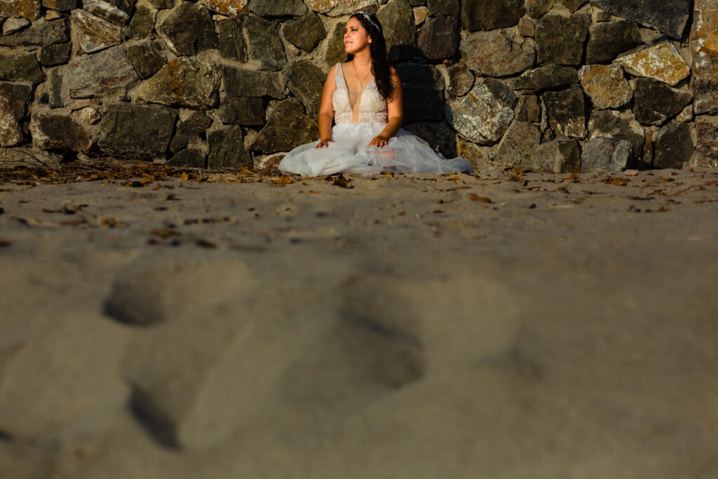 bride sit on the sand with a withe dress looking to the ocean 